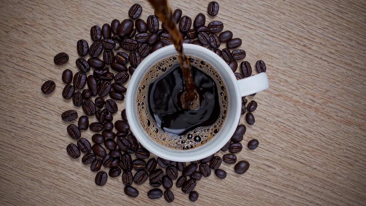 Frisk kaffe hældes i en hvid kop omgivet af ristede kaffebønner
