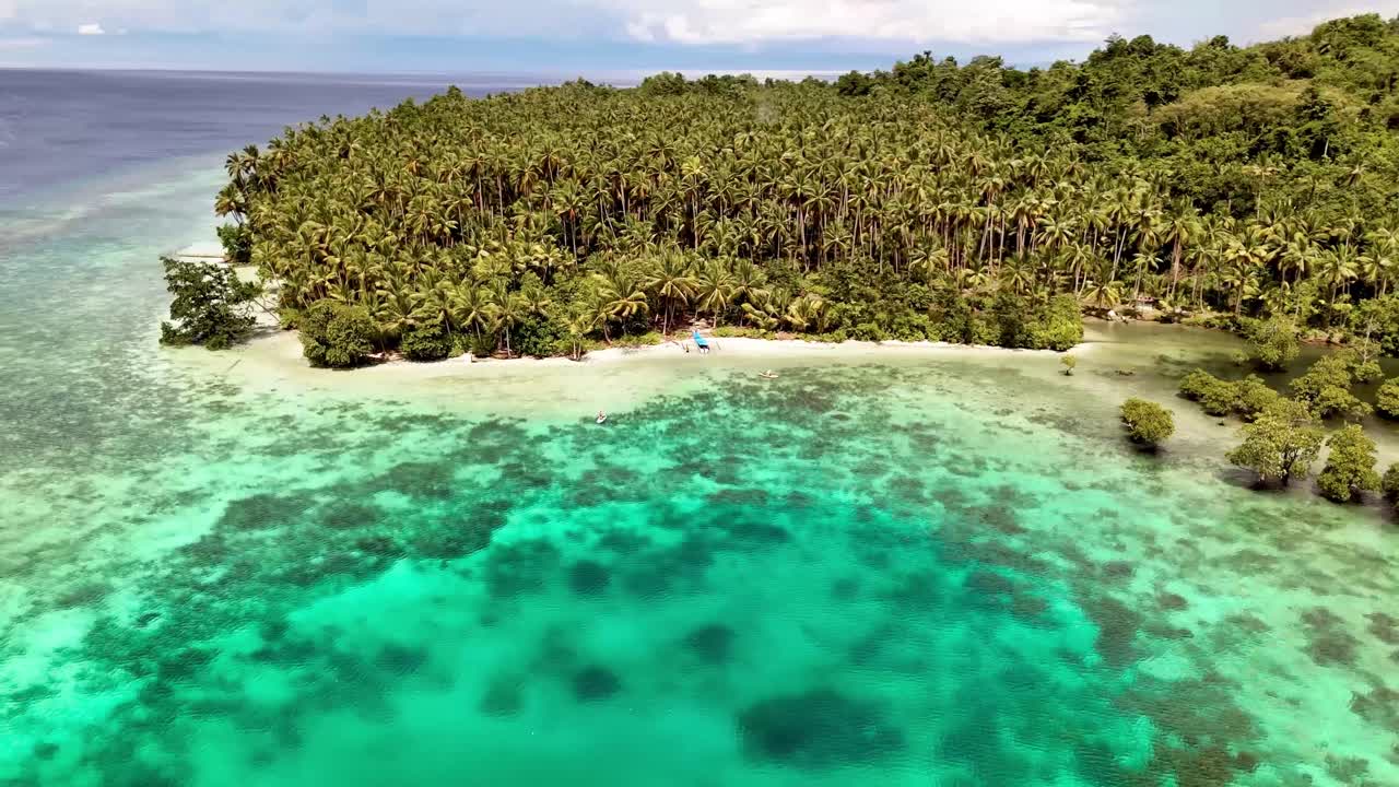 4K dronevideo af folk, der padler på paddleboards ud for kysten af en fantastisk tropisk ø i Banggai-øerne, Sulawesi, Indonesien. Øen er dækket af palmer med hvidt sand og blåt hav