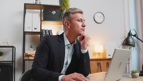 handsome young businessman thinking business ideas while sitting with laptop at home office desk