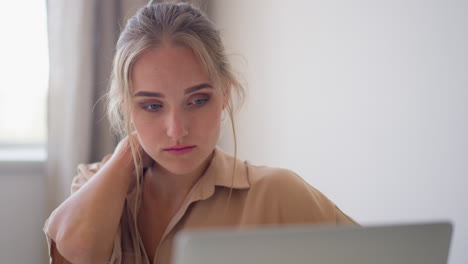 una joven rubia se siente cansada sentada en la oficina con una computadora portátil