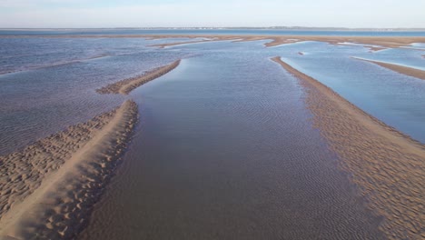 Ondulaciones-En-Las-Piscinas-Acuosas-Dejadas-Por-El-Océano-En-Una-Playa-De-Arena-Fría