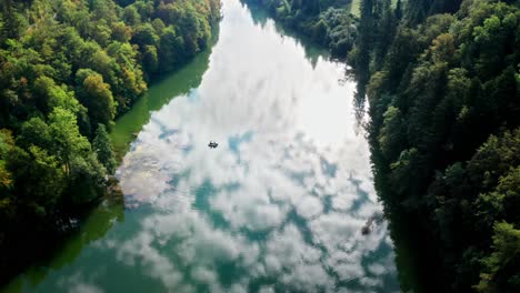 small fishing boat on reflecting water of river in middle of forest, drone aerial