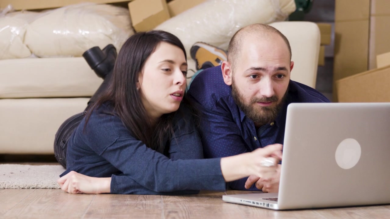 Young Couple Using Laptop While Moving Into New Home