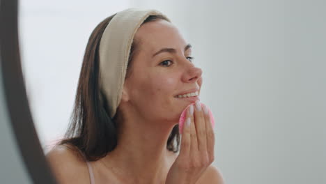 Positive-model-sponging-face-looking-mirror-home-closeup.-Woman-cleaning-pores