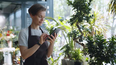 young entrepreneur touching tablet screen looking at flowers in florist's shop