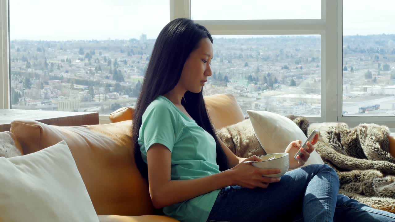 거실 4k에서 아침 식사를 하는 동안 휴대 전화를 사용하는 여성