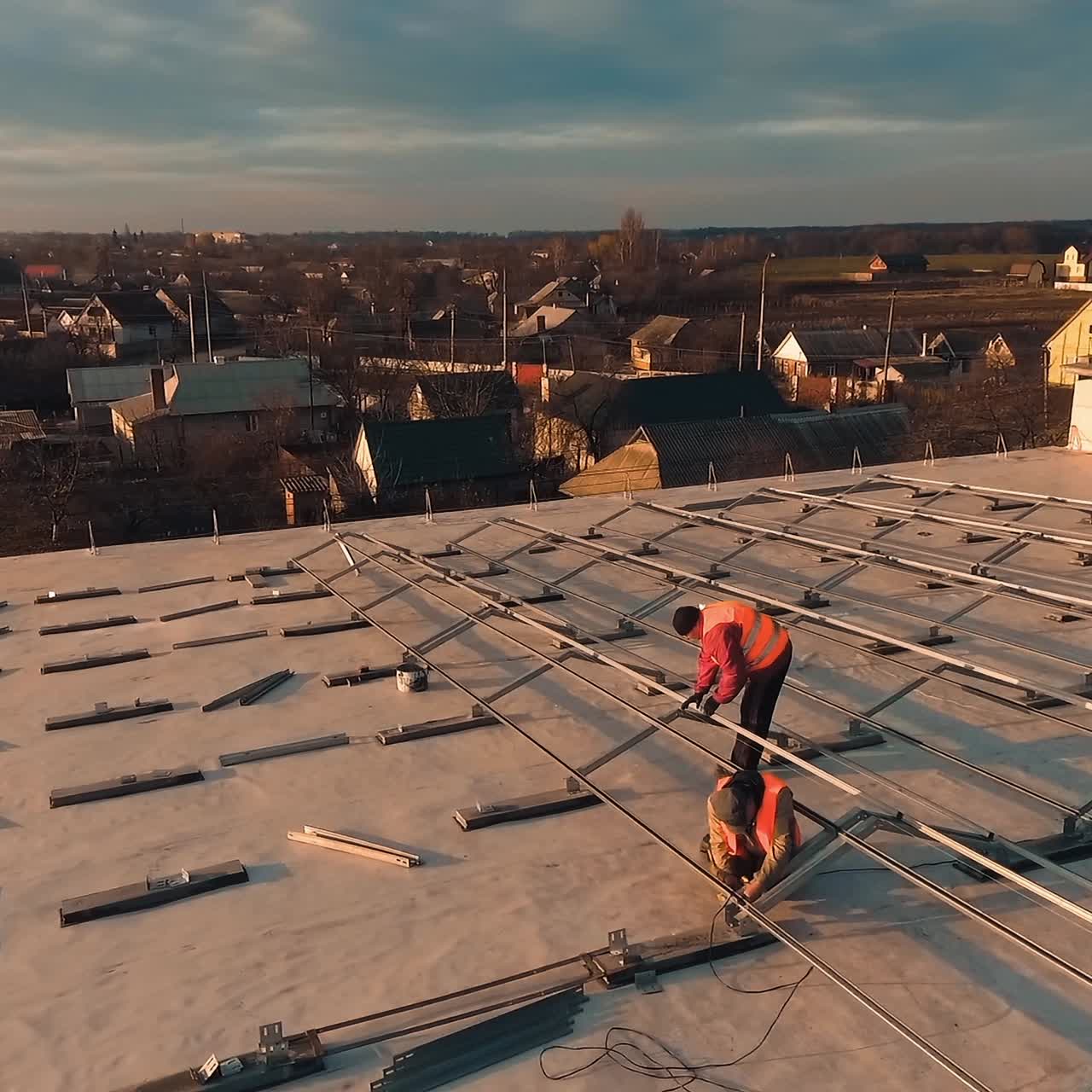 Installation solar panels at sunset. Workers in protective uniform making metal constructions on the roof of a building in the setting sun.