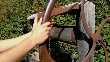 womans hand rotating wheel on old rusty water well, still