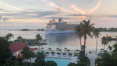 Massive-cruise-ship-docking-at-Bahamas-port,-static-view-from-a-balcony-of-a-hotel,-tropical-island-resort-with-pool-and-palm-trees,-Nassau-4K-30-FPS