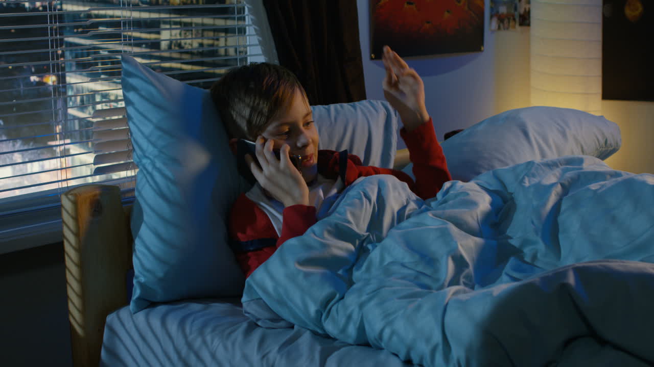 Young boy talking on a smartphone in his bed at night