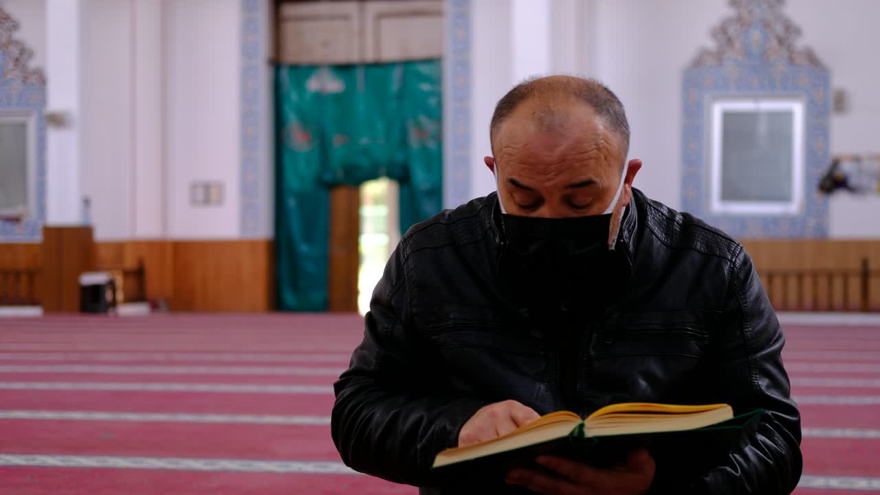 남자는 마스크를 쓰고 모스크에서 꾸란을 읽습니다.