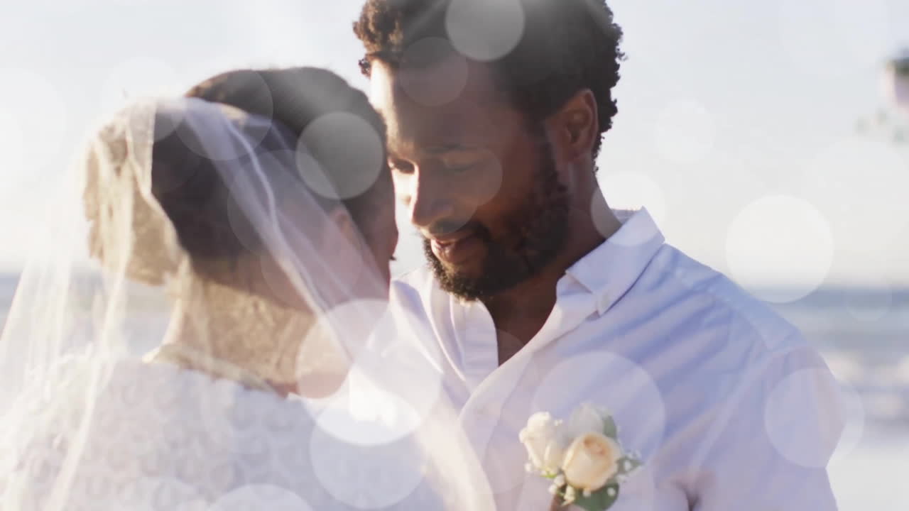 Animazione di punti luce sopra un felice sposo afroamericano che svela la sposa sulla spiaggia a un matrimonio