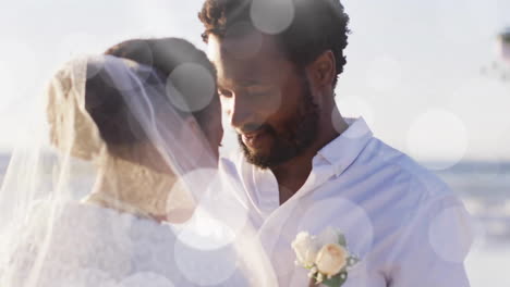 Animation-Von-Lichtpunkten-über-Einem-Glücklichen-Afroamerikanischen-Bräutigam,-Der-Die-Braut-Bei-Der-Hochzeit-Am-Strand-Enthüllt