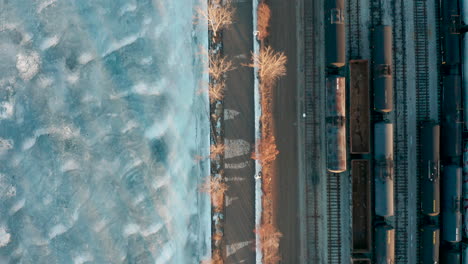 Aerial-shot-of-walking-path-between-train-yard-and-frozen-lake