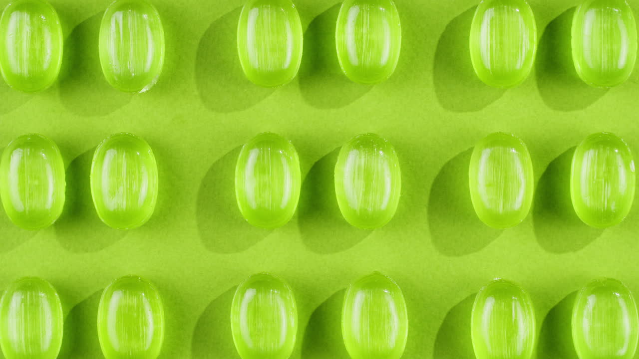 Green mint mentol lollipops, candies, bonbons disappear on purple background. Summer bright texture studio shot for store, supermarket, close up top view. Children favorite sweets made of sugar.