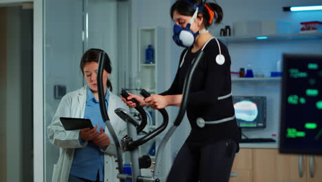 woman athlete with mask running on cross trainer in sports science lab