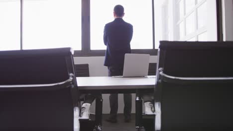 Vista-Trasera-De-Un-Hombre-De-Negocios-Senior-Mirando-Por-Una-Ventana-Desde-Su-Oficina-Moderna-En-Cámara-Lenta