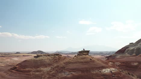 aerial of a man standing on rock on top of the hill with stunning view on desert landscape of utah usa, pull back drone shot