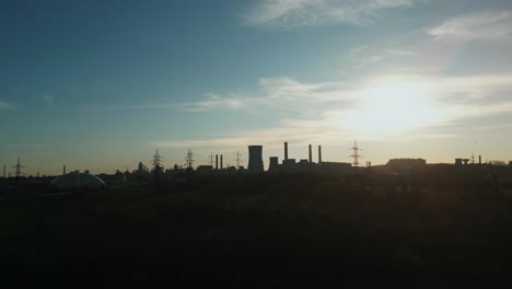 silhouette of cooling tower and smokestacks of steel factory on sunny afternoon in galati, romania. descending drone shot