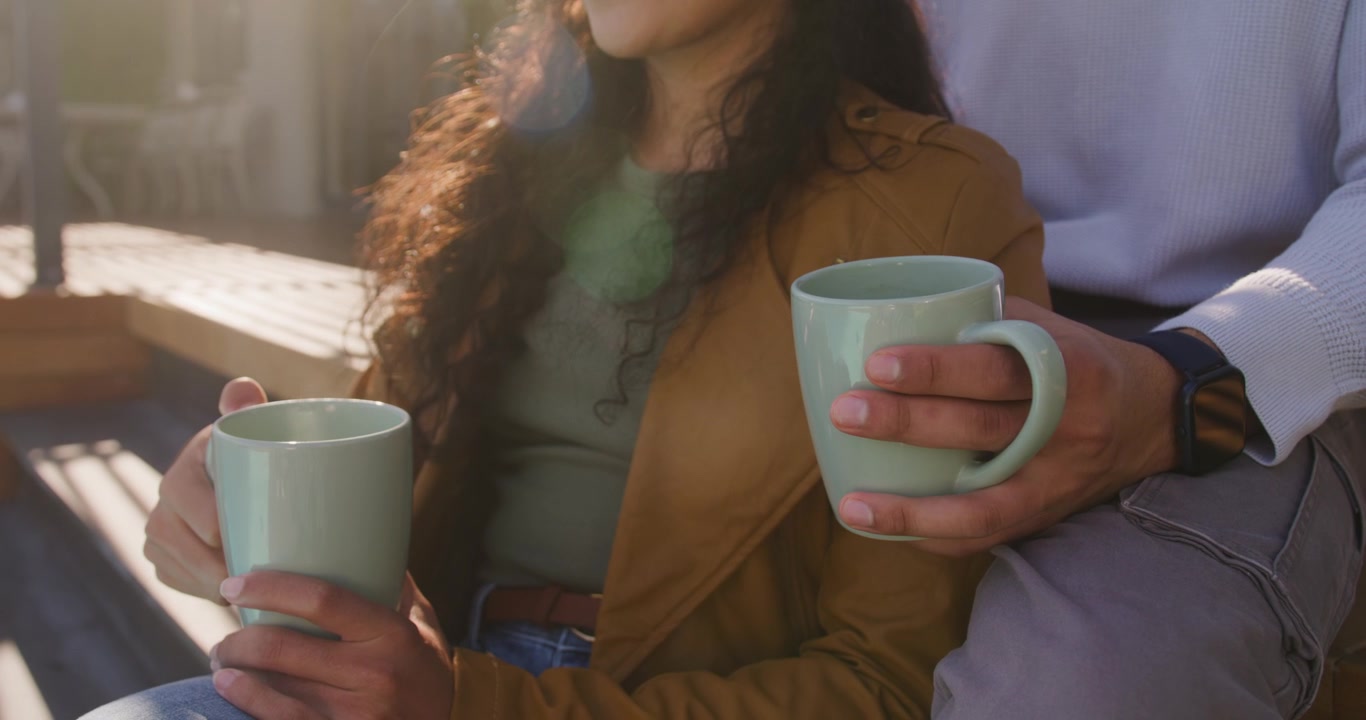 Coppia seduta sul ponte che tiene tazze color menta, la luce del sole in movimento rivela un cappotto color cammello