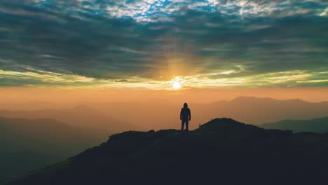 the man standing on the mountain top against the picturesque sunset