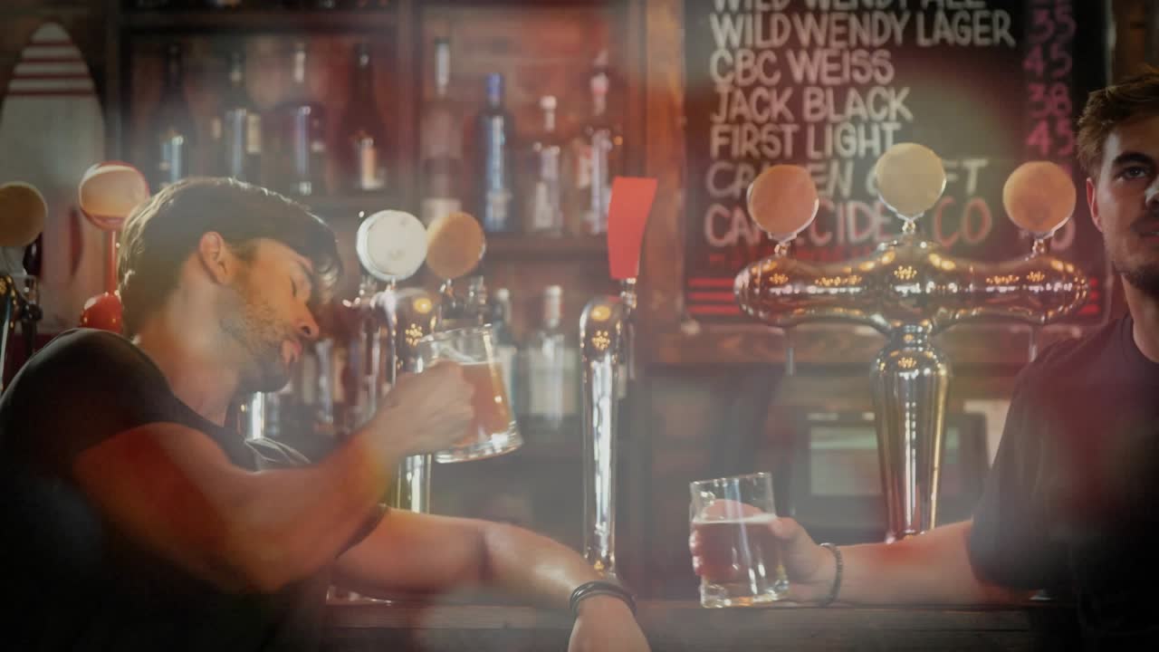 Male patrons responding to off-frame cue, right man leaning, left man drinking, bokeh over bar menu
