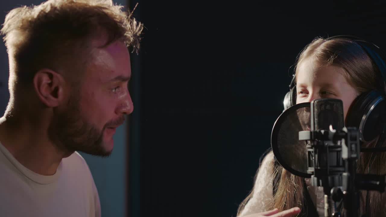 Child and bearded teacher join in song in musical studio. Skilled instructor shows sounds with fingers to cheerful little girl refining vocal prowess