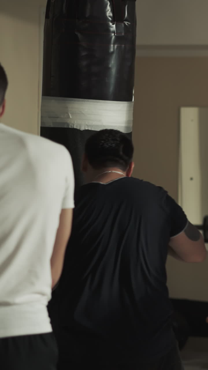 강한 남자 권투 선수는 특수 장비와 권투 가방을 사용하여 올바른 권투 기법을 수행합니다. 스포츠 클럽에서 그룹 연습.