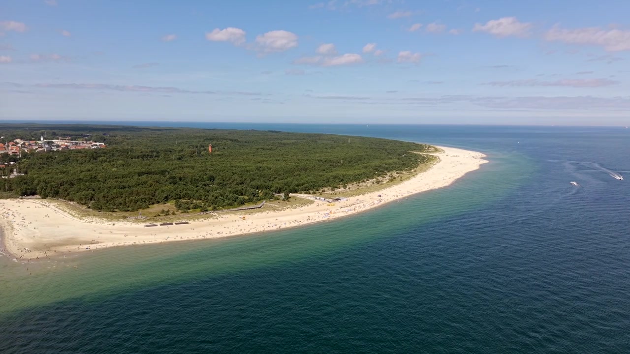 Høj droneoptagelse fra luften af spidsen af Hel-halvøen i Polen, den skovklædte odde omgivet af det turkise Østersø med sandstrande, en by blandt træerne og både på vandet på en solrig dag