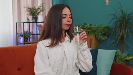 Una-Mujer-Joven-Sedienta-Sentada-En-Casa-Sosteniendo-Un-Vaso-De-Agua-Natural-Haciendo-Sorbos-Bebiendo-Agua-Sin-Gas