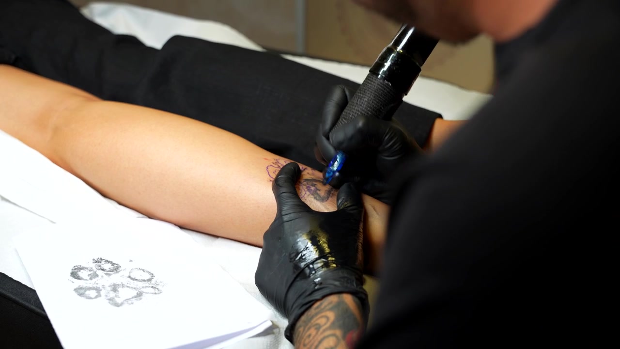 Tatuatore che disegna una zampa di cane e pulisce sulla pelle di una donna. Primo piano.