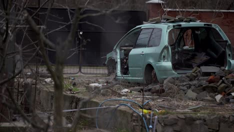 A-rusty-abandoned-car-in-the-parking-lot,-surrounded-by-a-fence-and-barbed-wire.-A-couple-of-cars-are-standing-in-a-sump-for-automotive-disassembly-or-metal-processing.-Restoration-of-a-retro-car.