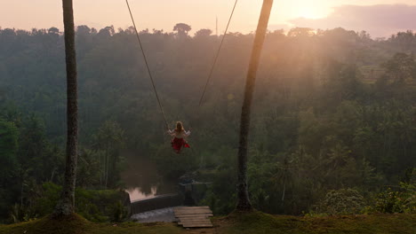 slow-motion-woman-swinging-over-tropical-rainforest-at-sunrise-travel-girl-sitting-on-swing-with-scenic-view-enjoying-freedom-on-vacation-having-fun-holiday-lifestyle