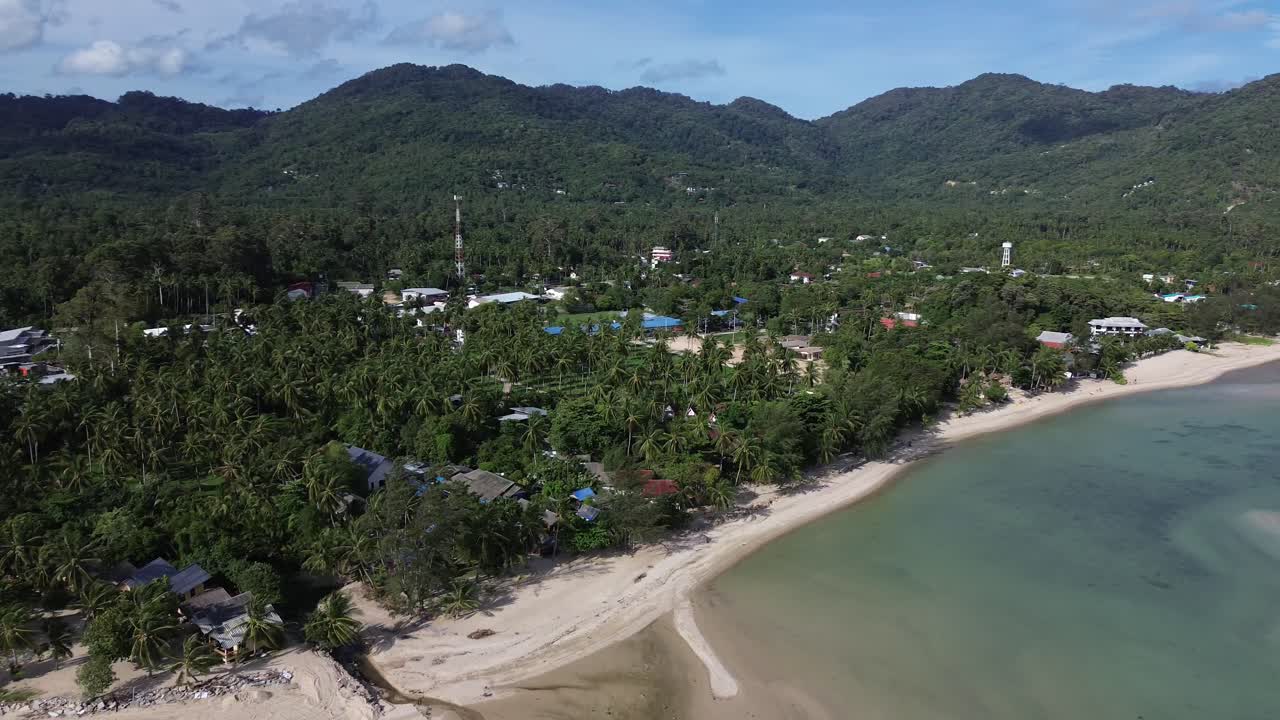 Editorial aerial drone footage of Baan Tai Beach on Koh Phangan island, Surat Thani, Thailand, showing tropical palm trees, seaside bungalows, sandy shoreline, and turquoise ocean water