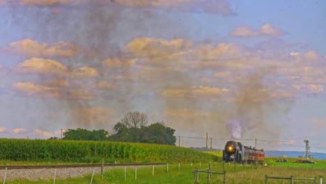 a view of a restored antique steam passenger train approaching blowing black smoke and steam on a sunny day