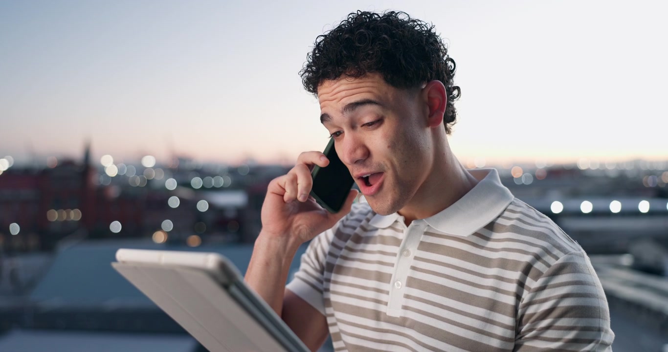 Giovane Uomo al Telefono mentre Usa un Tablet su un Terrazzo al Tramonto