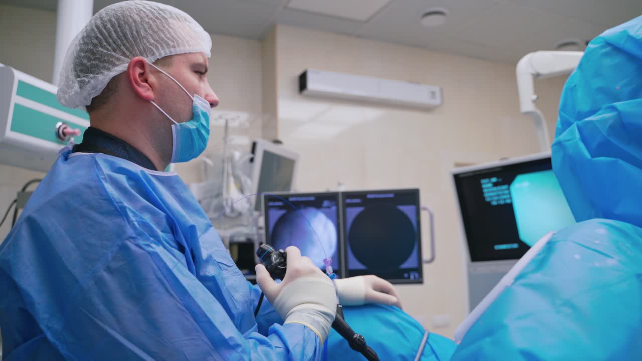 Specialist conducts laparoscopic surgery. Surgical operation with modern medical equipment in clinic. Side view of a doctor looking at the screen.