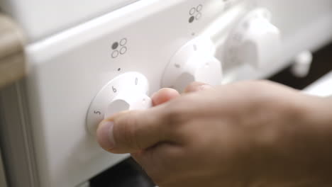 la mano masculina enciende la estufa a pleno calor usando la rueda de control, primer plano