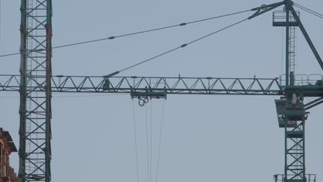 intersecting tower cranes with steel cables and hooks against the twilight sky at a construction site.