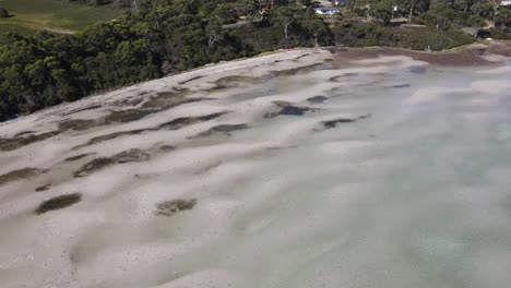 Drone-aerial-rise-and-pan-up-over-sandy-beach-with-houses-on-water-front-in-nature