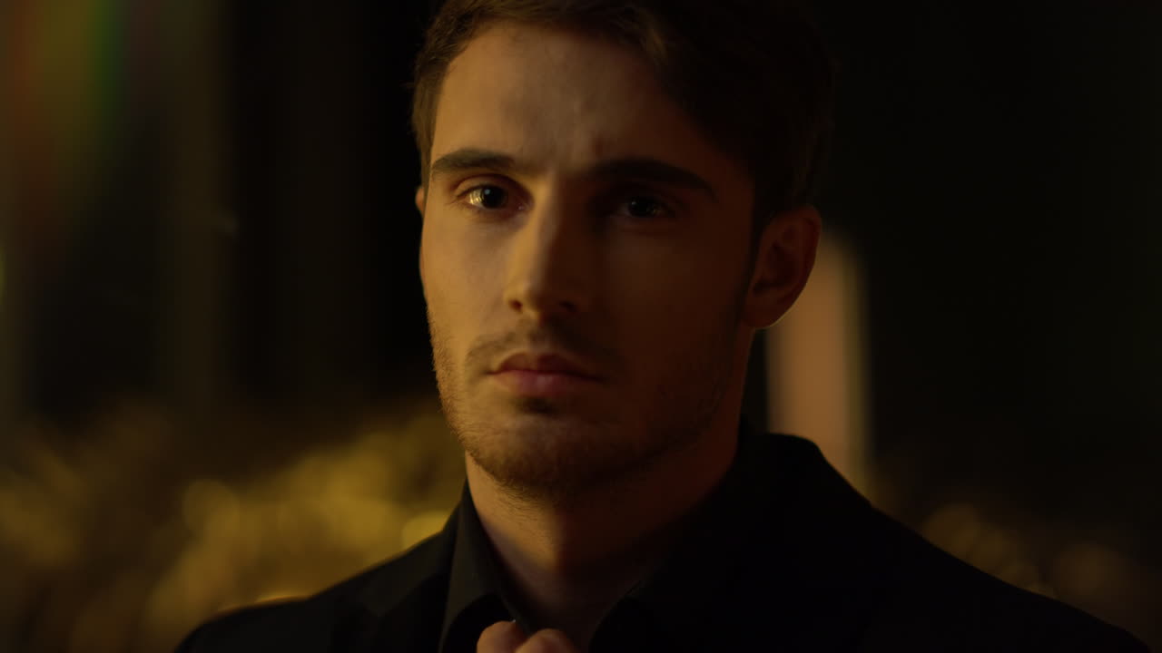 침착한 남자가 카메라를 들여다보고 있습니다. 매력적인 보스가 실내에서 목걸이를 똑바로  ⁇ 습니다.