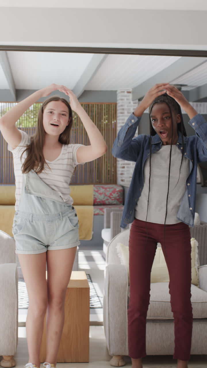 Vertical video of happy diverse teenage female friends making video blog in slow motion