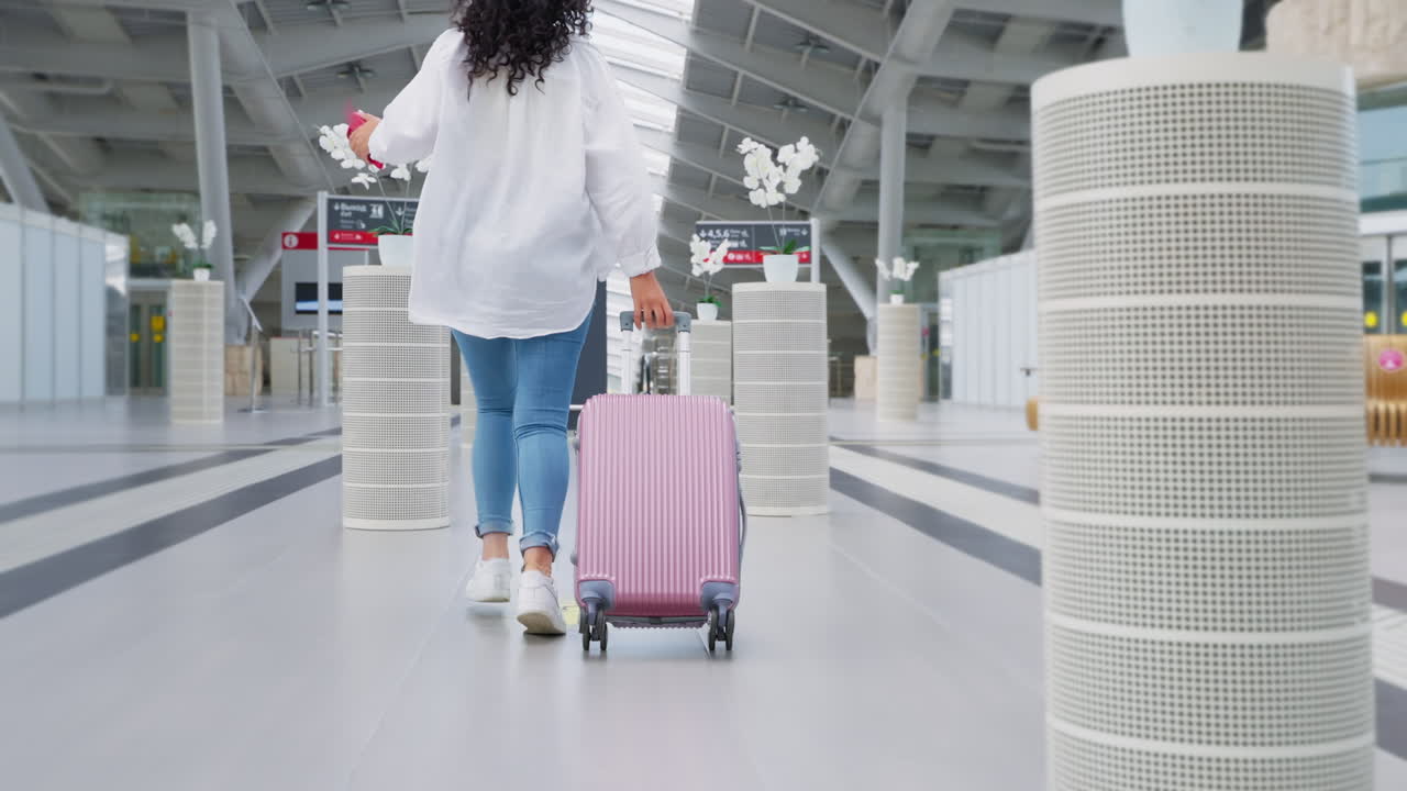 mujer con maleta rosa caminando por la terminal del aeropuerto