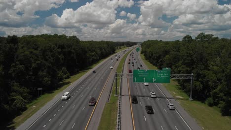 drone aerial pan up zdjęcie ujawniające autostradę i drogi samochody przejeżdżające przez niebieskie niebo białe chmury drzewa na boku autostrady