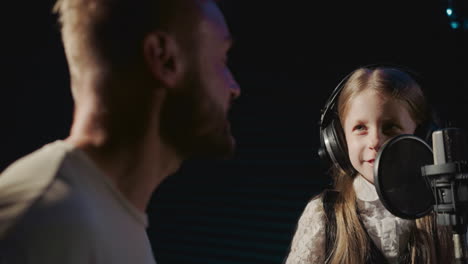 child and mentor sing in unison closeup. joyous young girl enhances vocal abilities with seasoned singer in sound record room. unfolding artistic talent