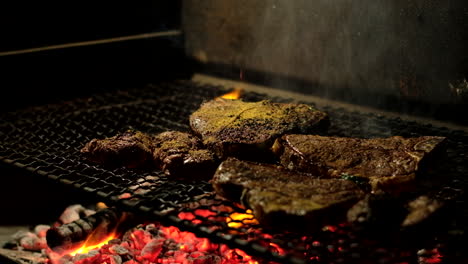 man spicing steaks on grid being grilled on hot coals of indoor fire