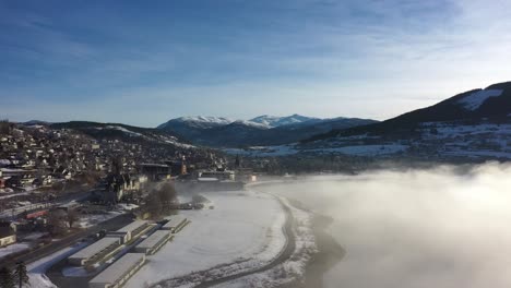 Ascending-aerial-revealing-Voss-during-beautiful-cold-morning-sunrise-with-frost-smoke-covering-lake-Vangsvatnet