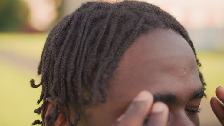 Soldato afroamericano che sistema i dreadlock all'aperto, soldato concentrato che si sistema i capelli all'aperto alla luce del sole, soldato all'aperto che si sistema attentamente l'acconciatura mentre si prepara per la missione alla luce del sole