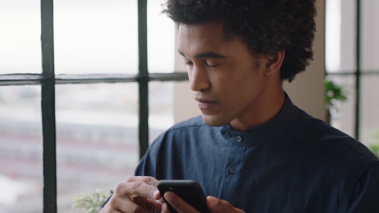 ritratto attraente uomo di razza mista che usa lo smartphone a casa godendo di una mattinata rilassata, navigando nei messaggi, mandando messaggi sui social media, guardando fuori dalla finestra, pianificando il futuro