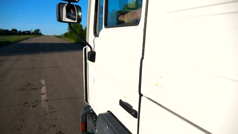 trucker in sunglasses reflecting in left side mirror of moving car. man driving lorry riding to destination through countryside road. cargo transportation concept. slow motion close up side view